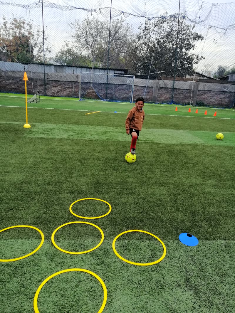 Alumno conduciendo el balón entre aros y conos en la cancha
