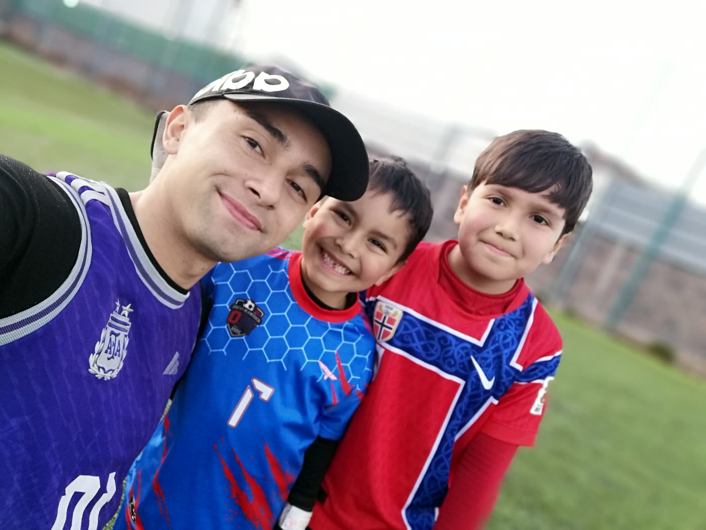 Matías Ortega sonriendo en una selfie con dos de sus alumnos en la cancha